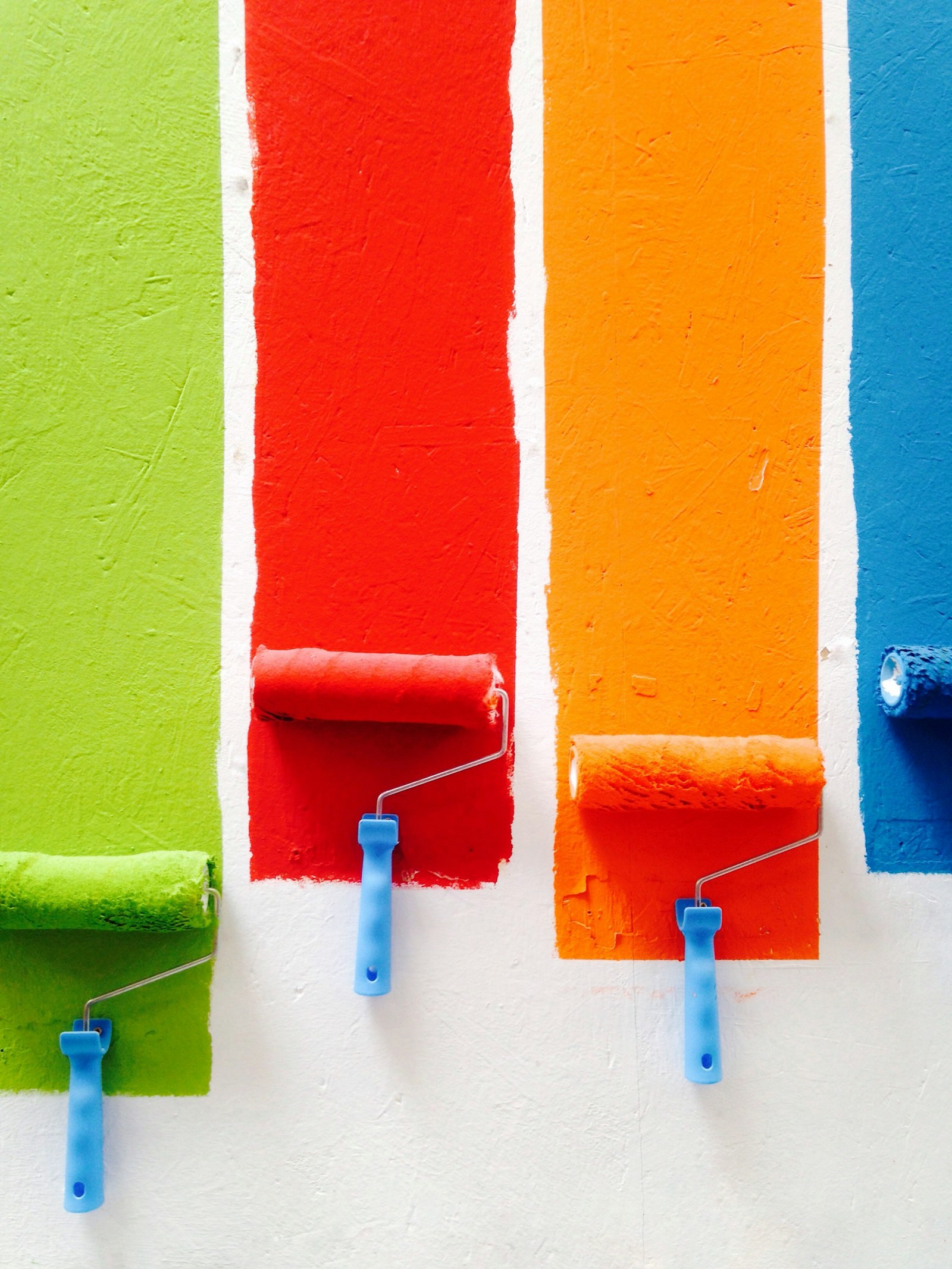 Bright paint rollers laying green, red, orange and blue stripes on a white wall